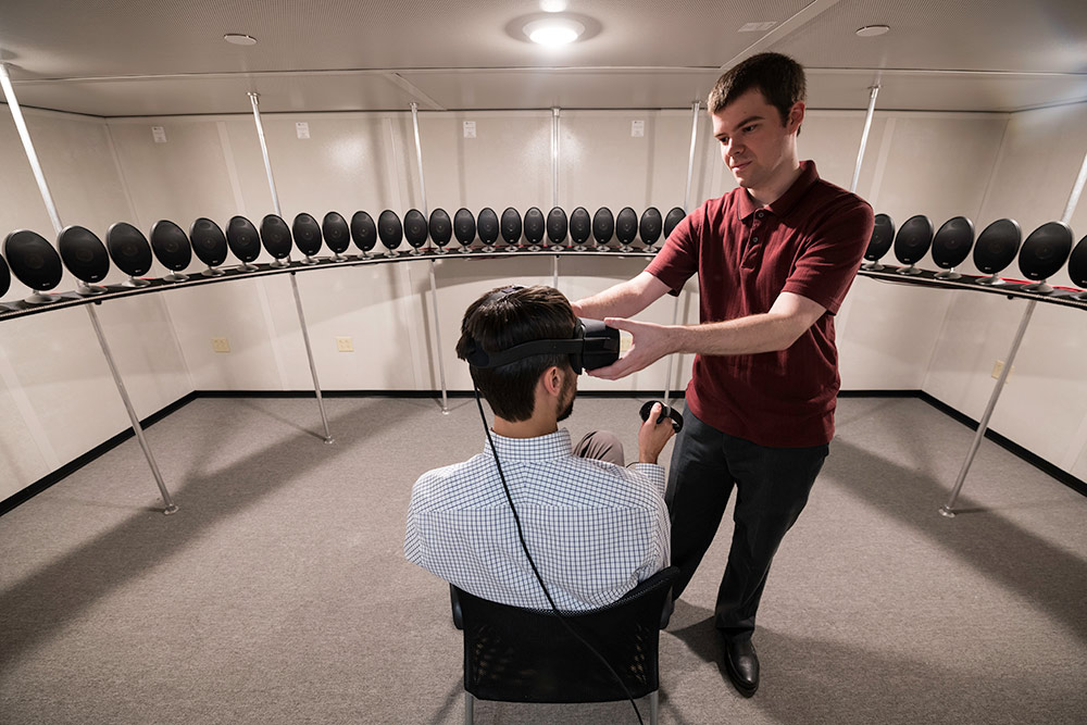 Biomedical engineering graduate student Tom Stoll, right, adjusts a virtual reality head-mounted display on assistant professor Ross Maddox. The array of speakers in Maddox's lab allows researchers to simulate realistic listening environments.