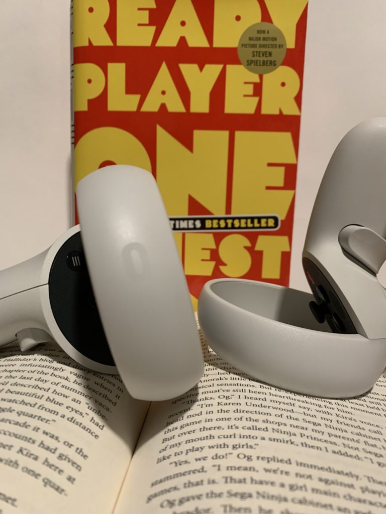 Image of the ready player one book and two oculus quest controllers set on top of another open book