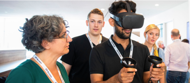 woman showing a man how to use a vr headset while an audience watches