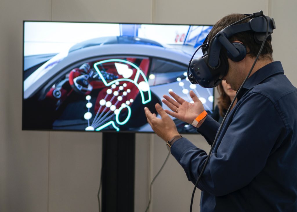 a man looking at his hands while wearing a vr headset with a tv screen behind him